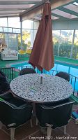 Full view of round terrazzo style patio table with brown umbrella and four patio chairs covered in green fabric covers