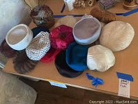 Photo showing entire assortment of 13 vintage women's hats on a table, varying in style, color, and material.