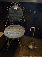 Front view of vintage metal vanity chair with blue tufted cushions and adjacent metal toilet paper holder.
