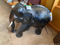 Side view of the dark wood carved elephant statue showing detail on the body, ears, and tusks.