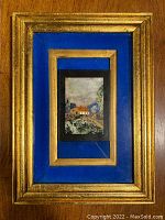 Front view of gilt wood frame with blue inset matting and the central pietra dura mosaic depicting a house in landscape.