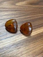 Top view of pair of triangular polished amber stone stud earrings showing translucent warm brown color and smooth finish.