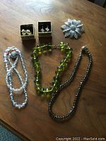Full lot overview showing three necklaces, two sets of earrings in boxes, and the brooch on a wooden table.