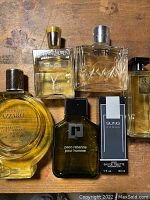Top-down view of seven cologne and perfume bottles on wooden surface, showing labels and caps for most bottles.