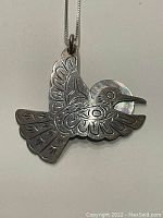 Front view of stylized hummingbird pendant with engraved details and mother of pearl circular accent