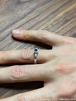 Ring worn on hand showing front view of deep blue gemstone set in sterling silver bezel on polished band.