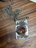 Pendant and chain laid flat on wood surface; full view of front design and chain length