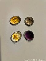 Overhead view of four faceted oval gemstones in yellow, smoky brown and purple.
