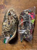 Two sealed plastic bags filled with mixed costume jewelry including faux pearl necklaces, metal chains, and colorful pendants.