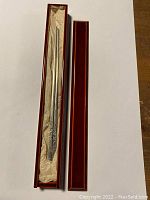 Pair of silver chopsticks in original lined box with lid adjacent on white background