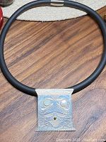 Front view of rectangular silver pendant on black rubber necklace, showing carved design and mother of pearl inlays.