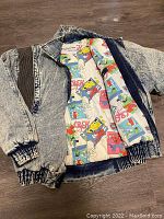 Acid wash denim jacket with comic book print lining visible inside, elastic cuffs, and waistband.