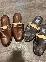 Two pairs of men's loafers on floor, showing brown leather pair and black textured leather pair with insoles visible