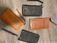 Overview of four leather zip wallets laid on floor, two tan and two black, showing exterior views and wrist straps