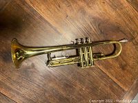 Full view of the trumpet laid flat on wooden surface showing the bell, valves, and general shape.