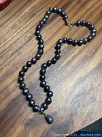 Full view of black pearl necklace laid out on wooden surface
