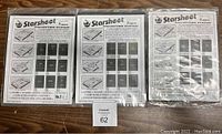 Three sealed packages of G&K Starsheet stamp collecting blanks, two style B02 and one style B03, shown front-facing on wooden surface.
