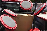 Close up of four red-rimmed electronic drum pads attached to frame, showing the black playing surface.