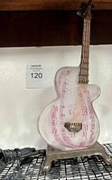 Front view of glass guitar lamp showing musical notes inside and attached to metal stand with power cord visible.