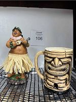 Front view of Hawaiian bobble figure and tiki mug on a checkered surface with white background