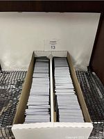 Photo of two long white cardboard card storage boxes filled with dense stacks of Magic The Gathering trading cards arranged vertically.