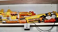 Photo showing a lineup of orange and yellow large Nerf blasters stacked horizontally on a shelf.