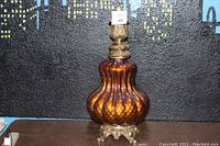 Full view of lamp body showing amber-colored ribbed glass base with brass decorative feet and socket holder.