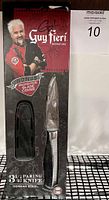 Packaging showing the knife inside with protective cover visible, Guy Fieri branding and key product details such as blade size and steel type.