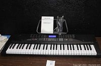 Front view of the MK-2100 keyboard, showing 61 full size keys, LCD display, control buttons, and included owner's manual and microphone.