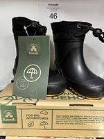 Pair of black Kamik kids boots showing waterproof rubber lower and quilted fabric upper with drawstring toggle closure, brand tag attached, size 4, new in box.