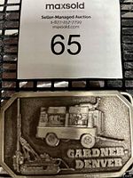 Photo showing front of vintage Gardner-Denver belt buckle with machinery and tank design.