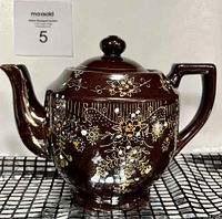 Front view of brown ceramic teapot with hand-painted white, orange, and gold floral designs.