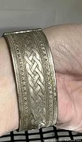 Close-up of vintage hinged oval cuff bracelet on wrist showing detailed raised Celtic knot pattern and decorative beaded borders.