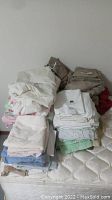 Photo of assorted bed linens stacked on a mattress showing variety of colors, patterns, and linens.