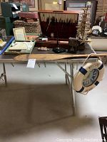 Overview of lot on table showing nautical items and calligraphy set including wooden paddle, model ship, life preserver, and wooden case.
