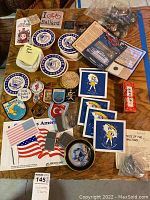Photo showing an assortment of travel souvenirs, U.S. Senate collector spoons, stickers, trivets, patches, and Asian novelties on a wooden table.