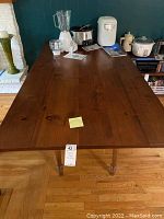 Full rectangular pine dining table with turned legs seen from an overhead angle, showing the wood surface and some other small appliances on top.