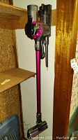 Dyson SV04 cordless vacuum mounted on wall showing full length with pink wand and gray body.