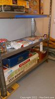 Full view of metal shelving with boxed board games including Monopoly, Anti-Monopoly, Rook, and game pieces with jar of marbles.