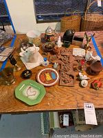 Collection of various home decor items on wooden table, featuring farm animal figurines, novelty plates, beer stein, brass items, and wooden knick knacks.