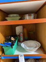 Two shelves showing vintage mixing bowls, bakeware items, and a green container holding kitchen utensils including whisks, peelers, and spatulas.