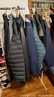 Seven men's jackets hanging on rack, various colors including quilted and fleece styles