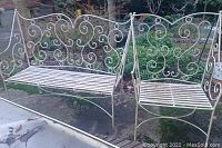 White metal outdoor bench with scrollwork design, slatted seat, and signs of weathering.