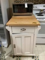 Frontal view of the white butcher block microwave stand with Sharp microwave on top showing drawer, cabinet door, and towel bars on side.