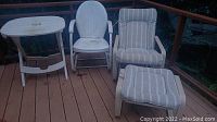 Overview photo showing vintage metal deck chair, striped padded glider chair, matching ottoman, and white plastic table on wood deck.