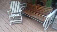 White wooden slat rocking chair positioned next to brown wooden slat metal frame glider bench on deck