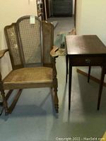 Wooden rocking chair with cane woven back and seat next to wooden side table with drawer and drop sides.