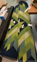 Two rolled area rugs with green and blue geometric chevron pattern visible along length.