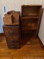 Photo of three wooden furniture pieces including an old chest of drawers with metal handles, a wooden shelf, and a handmade media holder with compartment dividers placed indoors on wooden floor.