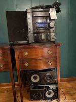 Full view of Sony stereo receiver stacked on furniture with coiled power cord on top, accompanied by two Magnavox speakers beneath.